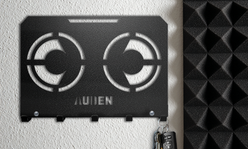 Metall-Schlüsselbrett mit geometrischem Schnittmuster und personalisiertem Namen, an einer strukturierten Wand montiert