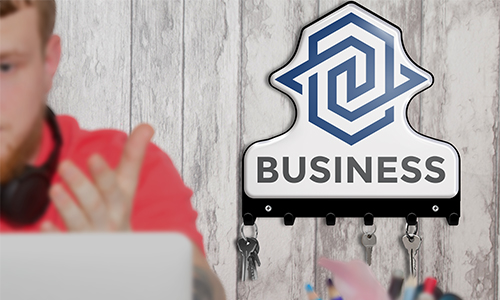 Person im roten Shirt am Laptop, Kopfhörer am Hals; Schlüsselhalter mit BUSINESS-Logo und Schlüsseln an der Wand