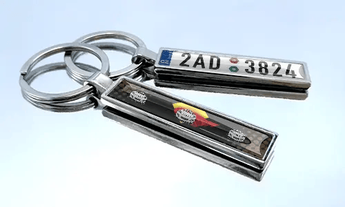 Kovový komiksový přívěsek na klíče s motivem auta a detailem registrační značky